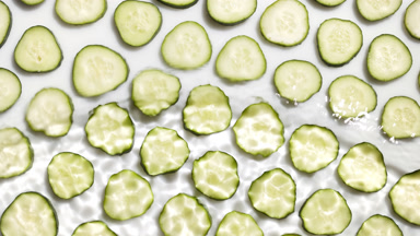 Wave flowing from bottom over cucumber slices on white bg