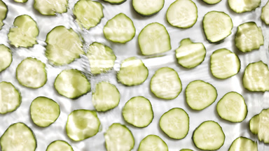 Water waves crossing and splashing over cucumber slices on white