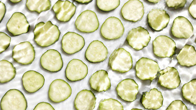Waves and ripples crossing over cucumber slices on white bg