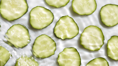 Waves crossing and splashing over cucumber slices on white bg