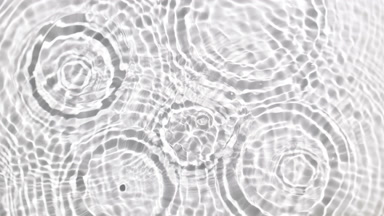 Drops falling in water making multiple water rings on white bg
