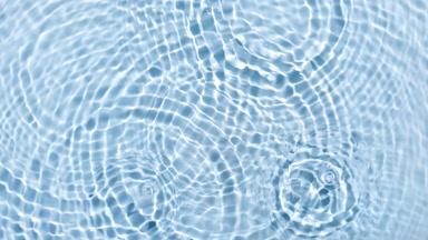 Water drops falling on water surface making circles on blue bg