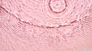 Wave makes ripples and splashes on water surface on pink bg