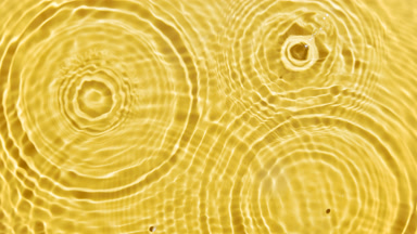Drops falling in water making multiple circles on yellow bg