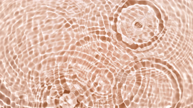 Drops fall down creating rings on water on beige background