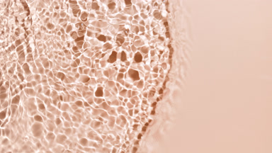 Wave makes splashes and ripples on water surface on beige bg