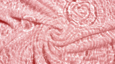 Drops fall down creating rings on rippling water on pink towel