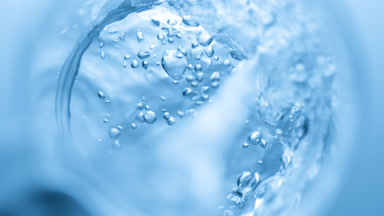 Transparent liquid pouring into beaker creates bursting bubbles