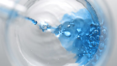 Blue liquid pouring into beaker with water creates bubbles
