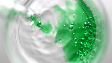 Green liquid pouring into beaker with water creates bubbles