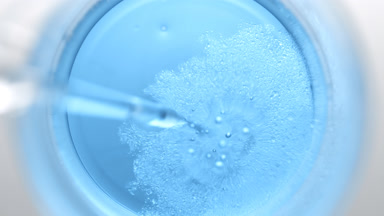 Dropper injects oil into blue liquid in beaker creating bubbles