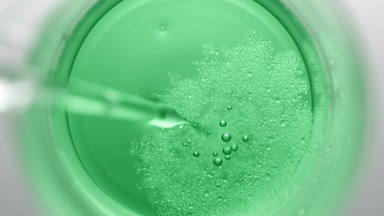 Dropper injects oil into green liquid in beaker creating bubbles