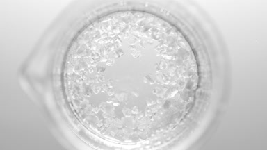 Crystals fall down into clear fluid in flask creating bubbles