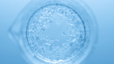Crystals fall down into clear fluid in flask creating bubbles
