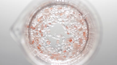 Crystals of brown salt fall down into liquid creating bubbles