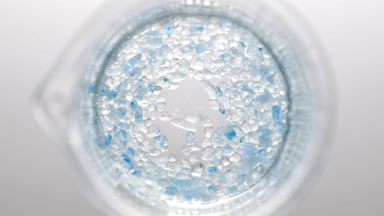 Crystals of blue salt fall down into liquid creating bubbles