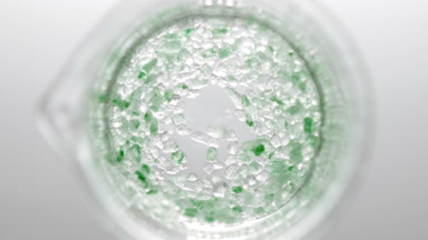 Crystals of green salt fall down into liquid creating bubbles