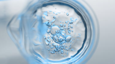 Light blue liquid pouring into beaker from flask creates bubbles