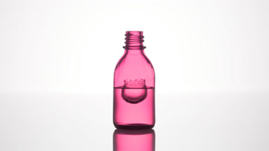 Drop falls into pink medical bottle with liquid creating splash