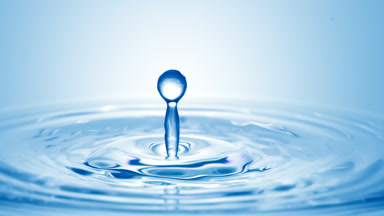 Blue drop falls down on surface of blue liquid creating circles