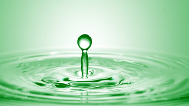 Green drop falls on surface of green liquid creating circles
