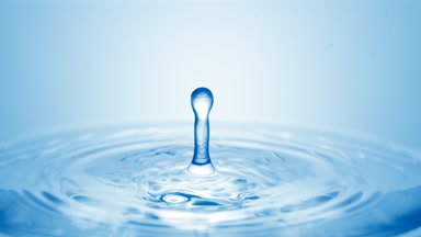Blue drop falls down on surface of clear fluid creating circles