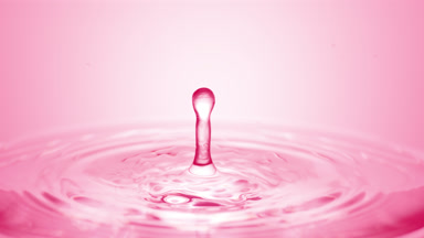 Pink drop falls down on surface of clear fluid creating circles