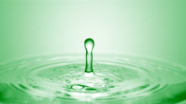 Green drop falls down on surface of clear fluid creating circles
