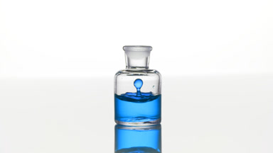 Blue tansy oil falls down into clear bottle with blue liquid