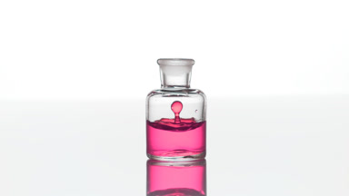 Rose oil falls down into clear bottle with pink liquid