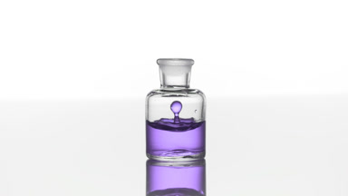 Lavender oil falls down into clear bottle with purple liquid