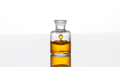 Argan oil falls down into clear bottle with yellow liquid