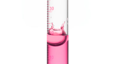Drop of pink fluid is falling down into graduated cylinder