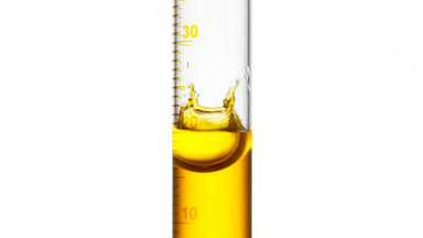 Drop of yellow fluid is falling down into graduated cylinder