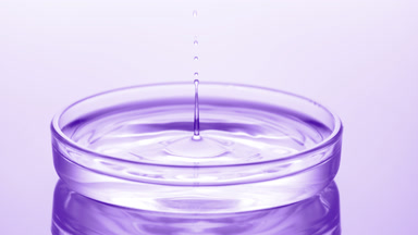 Drop of water falls into Petri dish with fluid creating ripples
