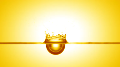 Yellow drop falls down on yellow liquid surface creating ripples