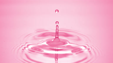 Water drop falls down on pink fluid surface creating water rings