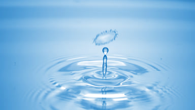 Drop of water falls on blue clear fluid creating circles on it