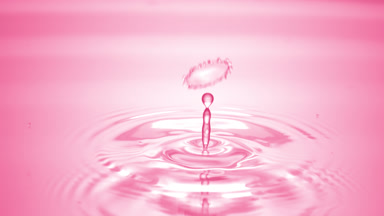 Drop of water falls on pink clear fluid creating circles on it