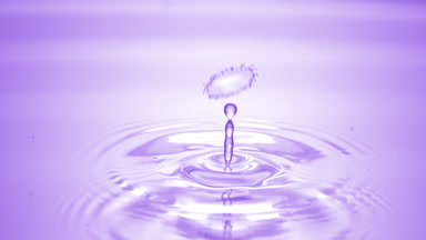 Drop of water falls on purple clear fluid creating circles on it