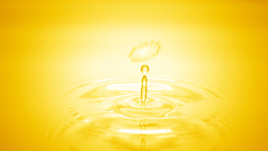 Drop of water falls on yellow clear fluid creating circles on it