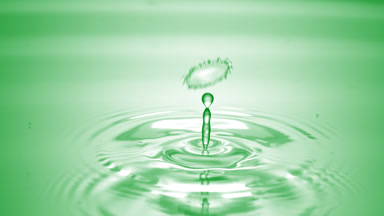 Drop of water falls on green clear fluid creating circles on it