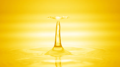 Drop of yellow fluid falls on fluid surface creating circles