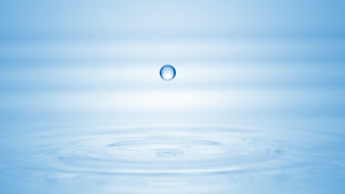 Drop of blue liquid falls on liquid surface creating circles