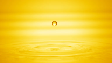 Drop of yellow liquid falls on liquid surface creating circles