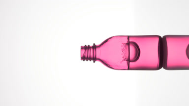 Drop falls into pink medical bottle with fluid creating splash