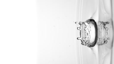 Grey drop falls down on surface of clear liquid creating circles
