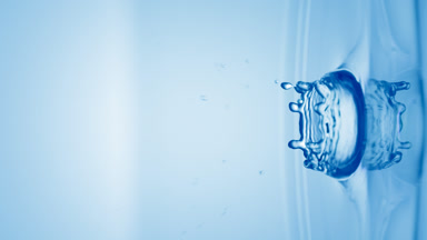 Blue drop falls down on surface of clear liquid creating circles