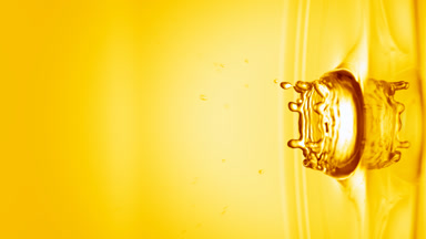 Yellow drop falls on surface of clear liquid creating circles