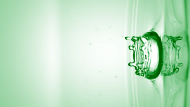 Green drop falls on surface of clear liquid creating circles